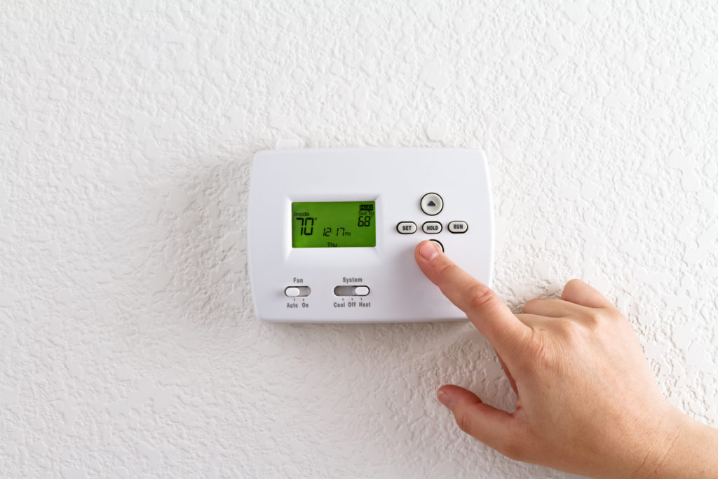 A person adjusting a thermostat that's currently set to 70 degrees.