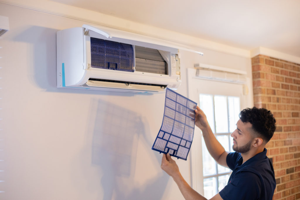 A man performs maintenance on an AC system on a wall.