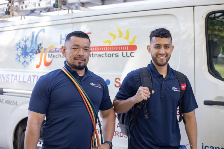 Two team members smiling in front of a "JC & JC HVAC Mechanical" truck.